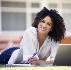 Student lying on grass outdoors studying with notebook